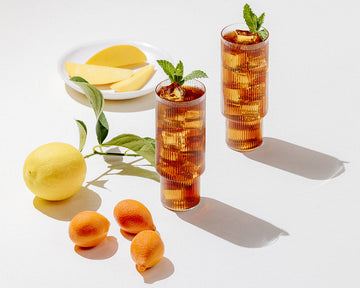 Two glasses of iced tea with fresh fruit placed next to them